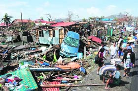 Residents walk past debris and destroyed houses along a road in Tacloban City in central Philippines on Sunday