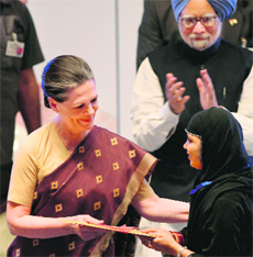 Congress chief Sonia Gandhi hands over documents to a bank account holder as PM Manmohan Singh looks on in Mumbai. 