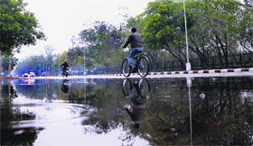A cyclist's reflection on still water creates an optical illusion following showers on Friday.