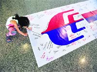 A young girl writes on a banner carrying messages for passengers of the missing Malaysian jetliner in Kuala Lumpur on Sunday