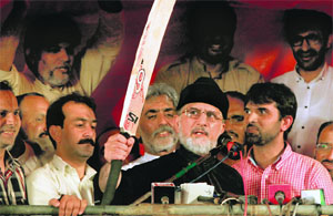 Tahirul Qadri raises a cricket bat while addressing supporters in front of Parliament House on Friday. He lacks mass appeal, but commands a dedicated set of followers. ReUTERS