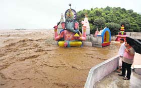 Residents look on from a roof as raging waters from the overflowing Tawi inundate a temple in Jammu on Saturday