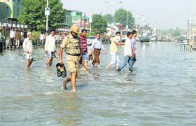A security man and employees walk through a flooded road near the Civil Secretariat in Srinagar on Thursday