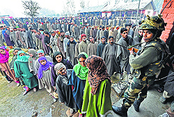 A security man stands guard as people queue up to cast their vote in Bandipora on Tuesday