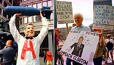 A demonstrator wearing a mask to the likeness of President Bill Clinton hoists a bomb over his head and (right) Lloyd Fillion joins other demonstrators downtown Boston on Friday as he carries a sign reading “impeach Clinton” during a protest against the US missile attacks in Sudan and Afghanistan.