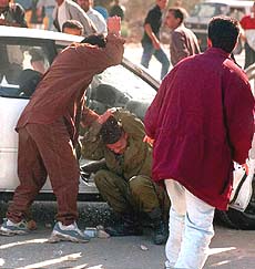 An Israeli soldier is beaten on the head by a Palestinian