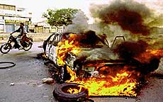 KARACHI : A motorcyclist passes a vehicle in flames after young activisits burn more than 100 vehicles to protest the killing of their political party leaders in Karachi on Wednesday. Entire neighborhoods of the port city have been shut down since Monday, following the shooting deaths of the leaders of the Muttiheda Qami Movement (MQM). AP/PTI