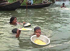 DHAKA : Kids swim through flooded water as they struggle to keep their food safe in Dhaka's Kamrangir Char on Thursday. Bangladesh has appealed to the international community for help.