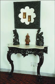 An intricately carved wooden mirror is hung to reflect two wooden faces on the opposite wall