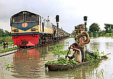 NARSINDHI, BANGLADESH: A resident rows a raft as a passenger train goes on a submerged railroad track near Narsindhi district, 40 km south of Dhaka on Sunday. Two months of floods in Bangladesh submerged 44 districts out of 64. 