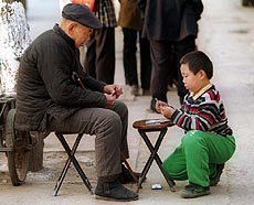 A young boy plays cards with his grandfather on a Beijing sidewalk. 