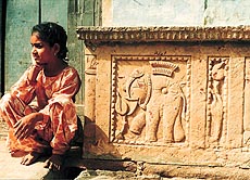 A girl sits beside a podium with an elephant motif carved on it.