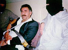 Kurdish rebel leader Abdullah Ocalan in handcuffs being flanked by masked officers while on a flight from Kenya to Turkey