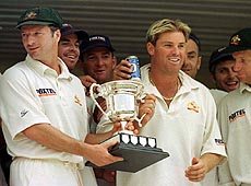Australian captain Stephen Waugh (left) holds the Southern Cross trophy with star leg spin bowler Shane Warne while their team mates celebrate after winning the inaugural test match against Zimbabwe