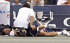 Carlos Moya of Spain, has his back stretched out by a trainer during his match against Nicolas Escude of France, at the U.S. Open tennis tournament in New York on Thursday. Moya later withdrew from the match