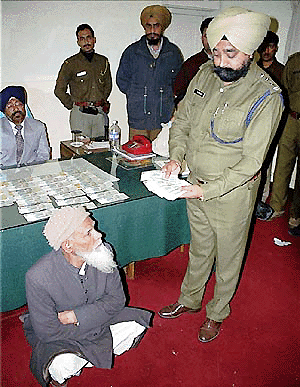 Indian Customs officer G.S. Oberoi (right) examines Wahid Ahmed (sitting) at the Attari railway station, near the India-Pakistan border, on Thursday. The police arrested Ahmed and two other men trying to smuggle in fake Indian currency. Ahmed’s bag contained fake notes worth more than Rs 99,000. —AP/PTI