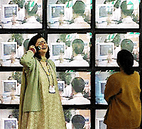 A woman talks on her cell phone as another stares at a multi-screen display at 'IT Asia 2000', an IT expo,which began in New Delhi on Tuesday.  — AFP