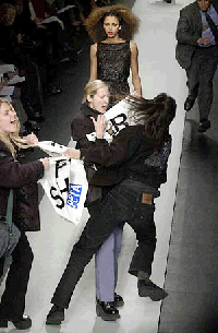A videographer tries to pull a sign away from anti-fur protesters after they jumped onto the runway during the presentation of Oscar de la Rentas Fall 2000 show, Tuesday, at Bryant Park in New York