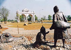 A statue of Bhai Kanhaiya offering water to enemy soldiers, against the backdrop of Anandpur Sahib gate