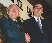 Matsushita Electric Industrial President Kunio Nakamura (R) and Hitachi Ltd President Etsuhiko Shoyama smile as they shake hands following a news conference in Tokyo
