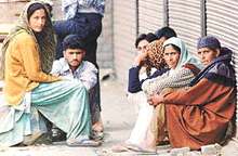 A Kashmiri family waits in front of closed shops, for the end of a nearby gunbattle in the village of Noorbagh in Sopore, 48 km north of Srinagar, on Wednesday. 