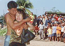 A knife-wielding man holds his blade to the chest of a woman in Bangkok as bystanders look on during the two-hour ordeal. 