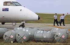 Australian pilots at Christmas Island airport wave as they walk past 13 life boat capsules with Australian Royal Navy markings.