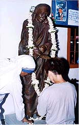 A nun touches the feet of a bronze statue of mother Teresa