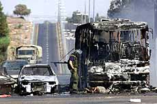 An Israeli policeman stands in front of a burned-out bus