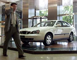 A South Korean businessman walks past a Daewoo Motor sedan, Magnus, displayed at the Daewoo Centre building in Seoul on Tuesday. 