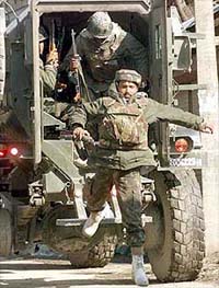 Army personnel jump out from an armoured vehicle
