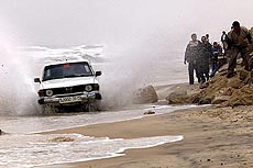A Palestinian drives his car as others walk on Gaza's coast to bypass Israeli checkpoints