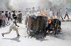 A rioter hits a burning rickshaw