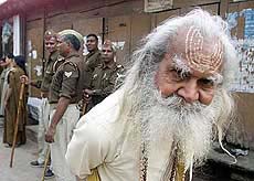 An elderly sadhu strolls past paramilitary force jawans