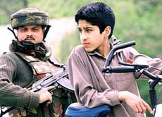 A soldier stands guard near a Kashmiri boy