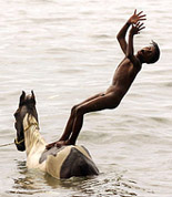 A young horse-keeper playfully jumps off his employers horse
