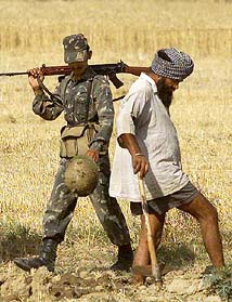 A soldier walks past a Sikh farmer