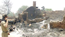 An Indian policeman stands beside a burnt house