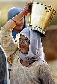 An elderly migrant carries a bucket of drinking water 