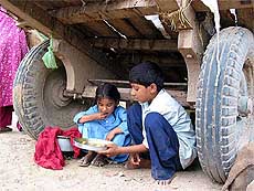 Uncertain about their future, children take their meal under the shade of a cart