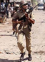 An armed paramilitary man runs through a riot-hit street 