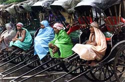 Rickshaw-pullers cover themselves with plastic sheets