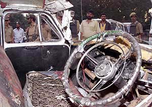 Policemen and local people stand besides a damaged car 