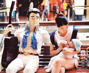 A life-size model of Elvis Presley with his guitar seems to be looking at a Thai woman feeding her child outside a shopping mall in the Thai resort town of Pattaya, Bangkok.