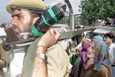 Policeman guards as Kashmiri villagers listen to an election candidate