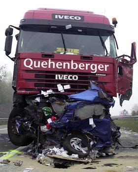 A truck stands behind a crushed car