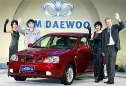 GM Daewoo Auto & Technology (GM Daewoo) president and CEO Nick Reilly, GM Daewoo's South Korean factory worker Kim Hyun-woo and promotional girls wave next to new model
