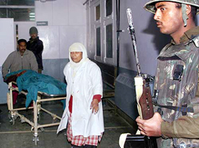 A paramilitary trooper stands guard as Kashmiri paramedics push a stretcher