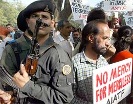 An armed guard stands watch as activists from the All-India Anti-Terrorist Front hold a demonstration