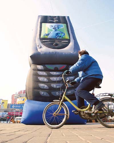 A Chinese woman rides a bicycle past a giant inflatable mobile phone model in Beijing